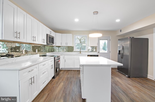 kitchen with pendant lighting, appliances with stainless steel finishes, white cabinetry, dark hardwood / wood-style floors, and a center island