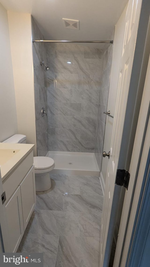 bathroom featuring vanity, a tile shower, and toilet