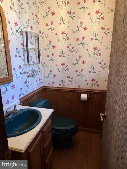 half bathroom featuring wallpapered walls, a wainscoted wall, and vanity