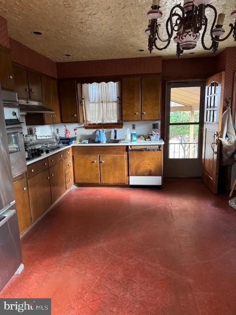 kitchen featuring appliances with stainless steel finishes, light countertops, dark floors, brown cabinets, and under cabinet range hood