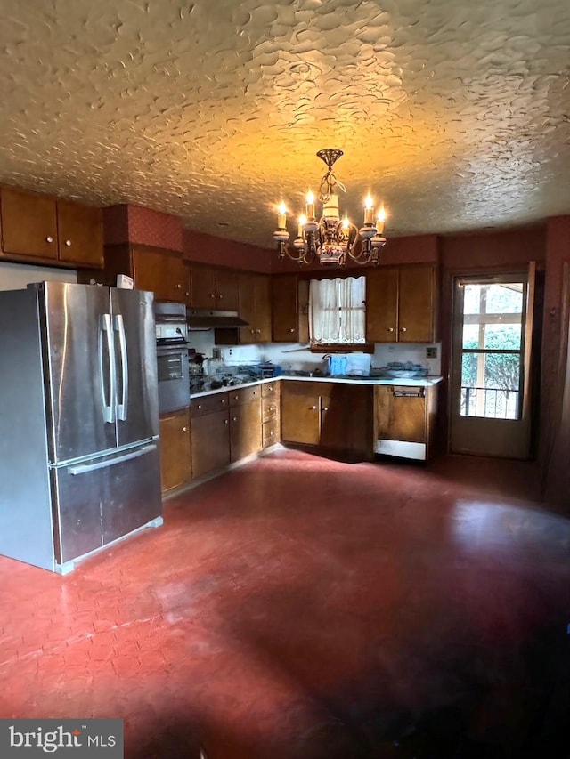 kitchen with freestanding refrigerator, a chandelier, decorative light fixtures, brown cabinets, and under cabinet range hood