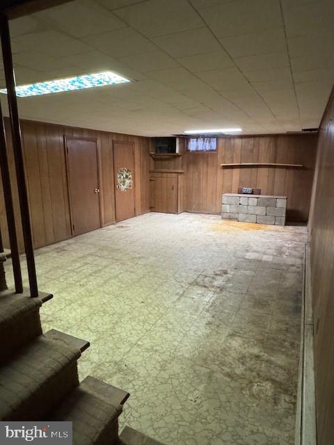 finished below grade area featuring a paneled ceiling, wood walls, and tile patterned floors