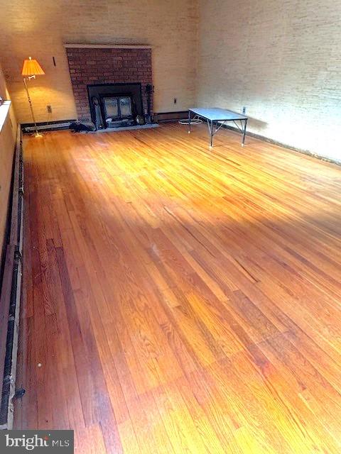 unfurnished living room featuring a baseboard radiator, wood finished floors, and a brick fireplace