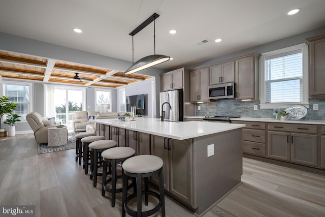 kitchen with pendant lighting, a healthy amount of sunlight, a large island, appliances with stainless steel finishes, and coffered ceiling