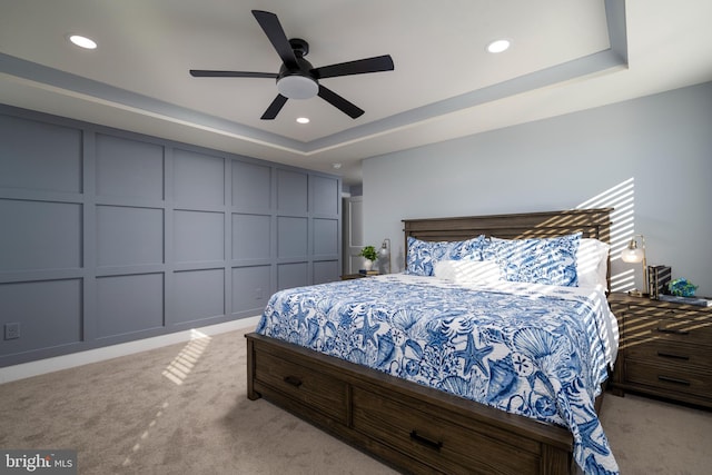 carpeted bedroom with ceiling fan and a tray ceiling