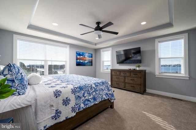 bedroom featuring ceiling fan, a tray ceiling, and light carpet