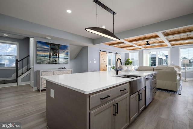 kitchen featuring coffered ceiling, a barn door, an island with sink, light wood-type flooring, and decorative light fixtures