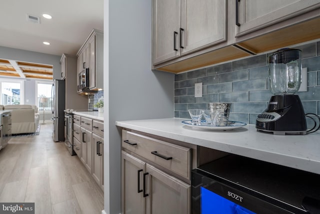 kitchen with light wood-type flooring, backsplash, light stone counters, and appliances with stainless steel finishes