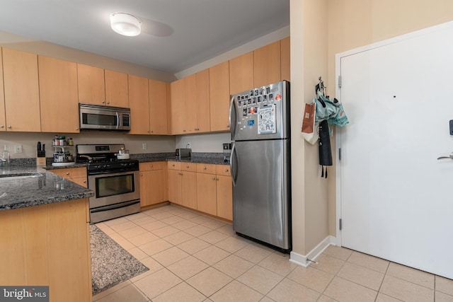 kitchen with dark stone countertops, stainless steel appliances, light tile patterned floors, light brown cabinets, and sink