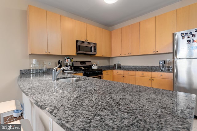 kitchen with appliances with stainless steel finishes, kitchen peninsula, dark stone counters, light brown cabinetry, and sink