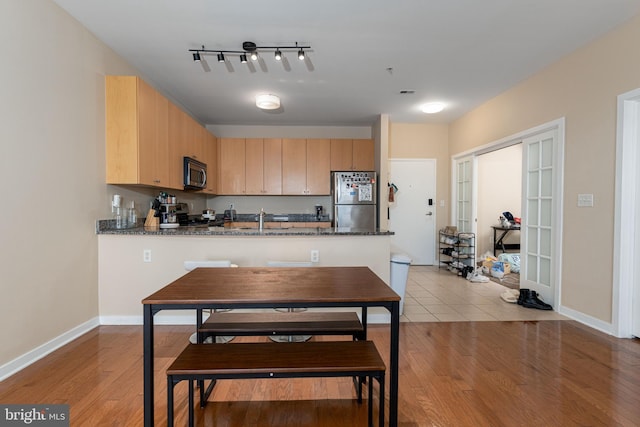 kitchen with appliances with stainless steel finishes, dark stone counters, light brown cabinetry, and kitchen peninsula