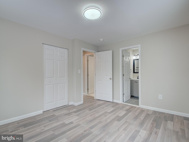 unfurnished bedroom featuring a closet, ensuite bathroom, and light hardwood / wood-style flooring