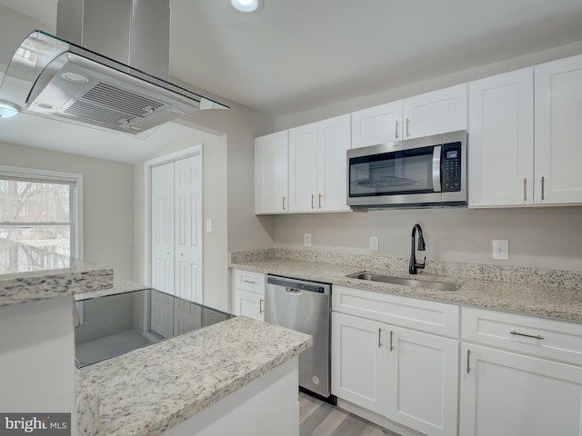 kitchen featuring appliances with stainless steel finishes, range hood, sink, and white cabinets