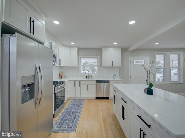 kitchen with appliances with stainless steel finishes, white cabinetry, sink, light stone counters, and light hardwood / wood-style floors