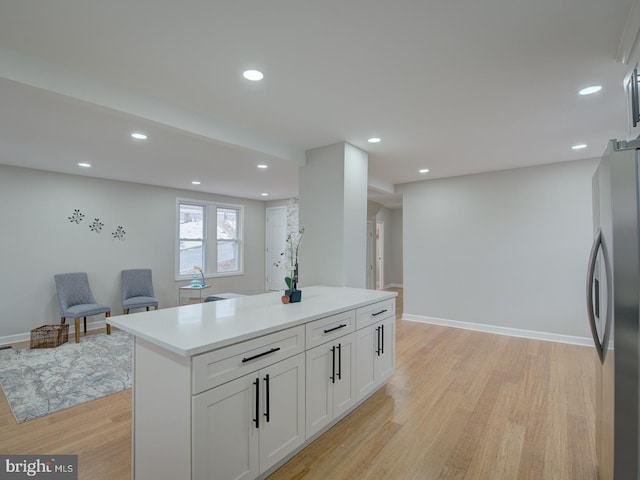 kitchen featuring stainless steel refrigerator, white cabinetry, a kitchen island, and light wood-type flooring