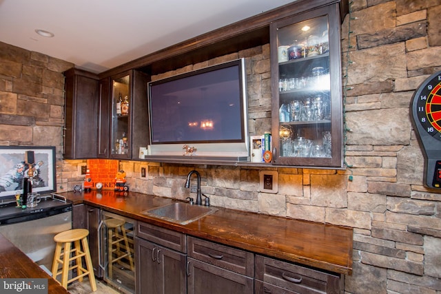 bar featuring sink, dark brown cabinetry, and fridge