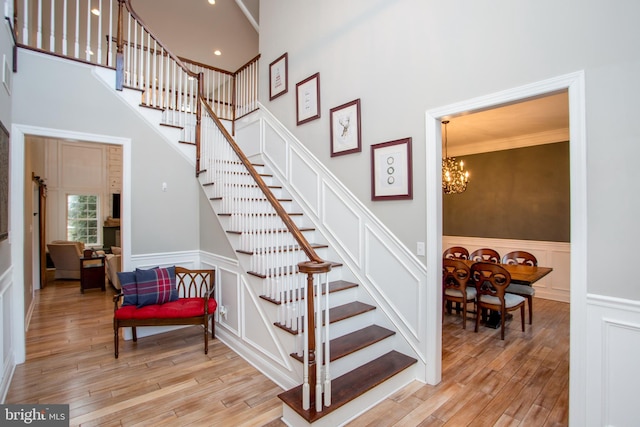 staircase with wood-type flooring, a towering ceiling, a chandelier, and ornamental molding