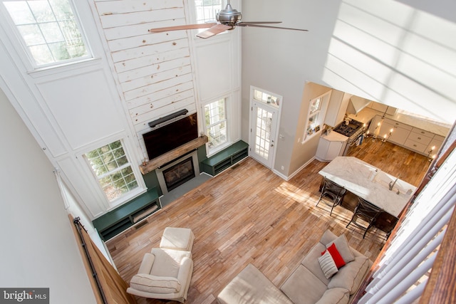 living room with ceiling fan, a towering ceiling, sink, and light hardwood / wood-style flooring