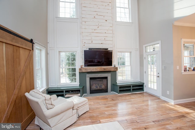 living room with light hardwood / wood-style flooring, ornamental molding, a barn door, and a towering ceiling