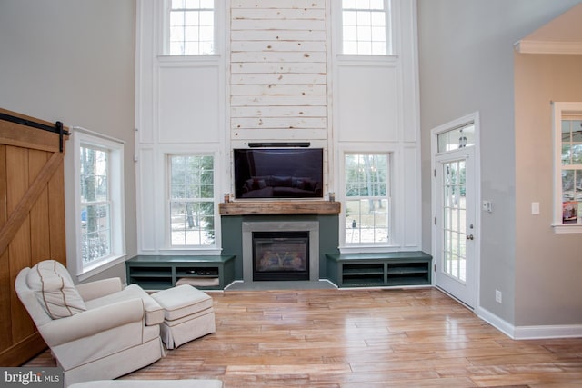 living room with a high ceiling, a wealth of natural light, ornamental molding, and light hardwood / wood-style flooring