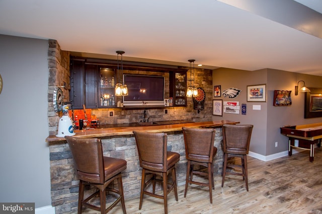 bar featuring butcher block countertops, wood-type flooring, decorative backsplash, sink, and hanging light fixtures