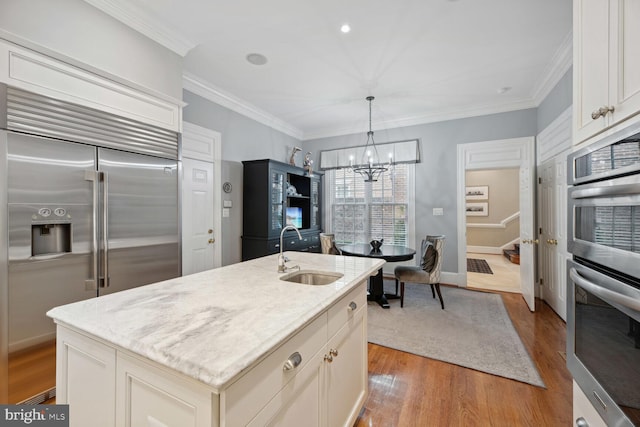 kitchen featuring an island with sink, sink, light hardwood / wood-style floors, stainless steel appliances, and light stone countertops