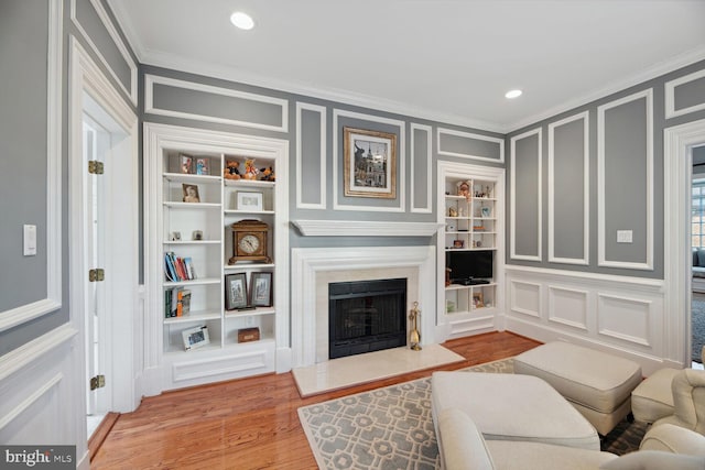 living room featuring built in shelves, crown molding, and light wood-type flooring