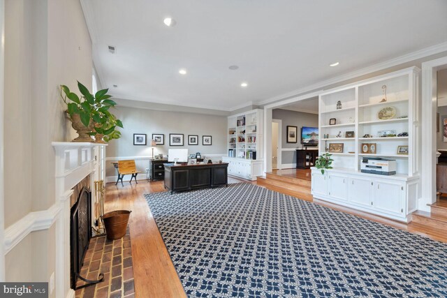 living room featuring built in shelves, ornamental molding, and light wood-type flooring