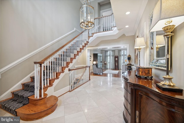 tiled entrance foyer featuring crown molding, a towering ceiling, and a chandelier