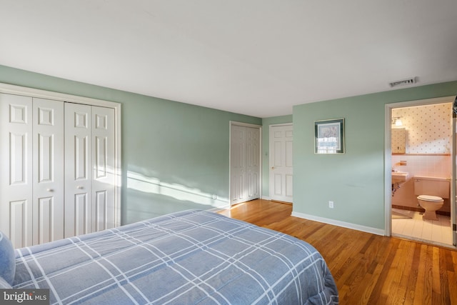 bedroom with baseboards, visible vents, connected bathroom, wood finished floors, and multiple closets