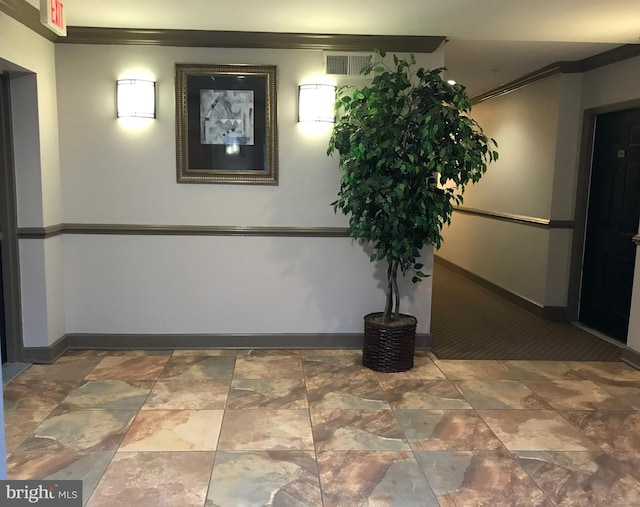 hall with ornamental molding, stone finish flooring, visible vents, and baseboards