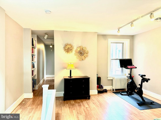 exercise room featuring radiator, track lighting, baseboards, and wood finished floors