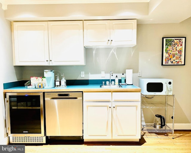 kitchen featuring white microwave, beverage cooler, a sink, white cabinets, and dishwasher