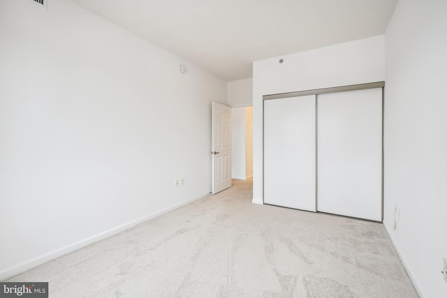 unfurnished bedroom with light colored carpet and a closet