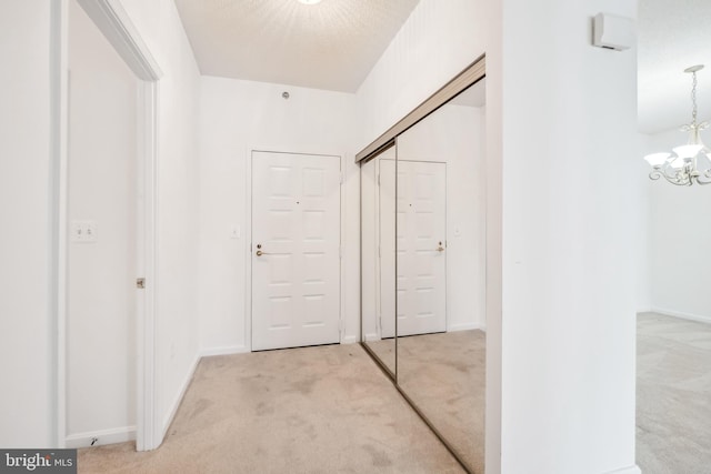 corridor with a textured ceiling, light colored carpet, and a chandelier