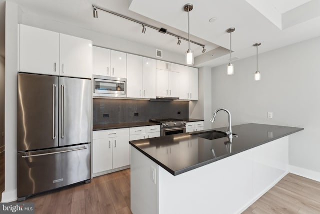 kitchen featuring kitchen peninsula, high end appliances, pendant lighting, white cabinets, and sink