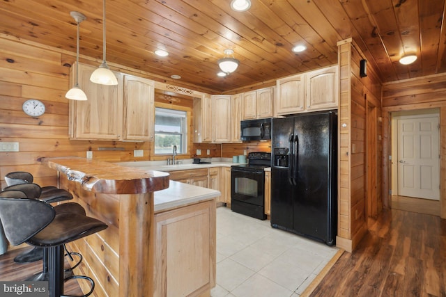 kitchen with light brown cabinetry, decorative light fixtures, black appliances, and wooden walls