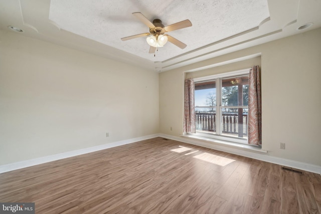 spare room featuring hardwood / wood-style flooring, a textured ceiling, a raised ceiling, and ceiling fan