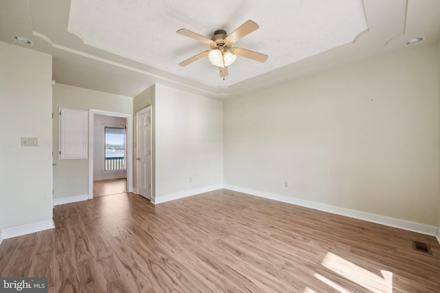 spare room featuring ceiling fan, a tray ceiling, and light hardwood / wood-style flooring