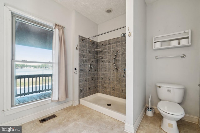 bathroom featuring a textured ceiling, tiled shower, and toilet