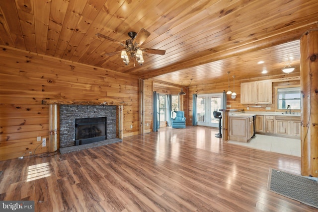 unfurnished living room with a fireplace, light hardwood / wood-style floors, wooden walls, and sink