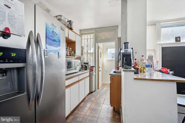 kitchen featuring stainless steel fridge, white cabinetry, and kitchen peninsula