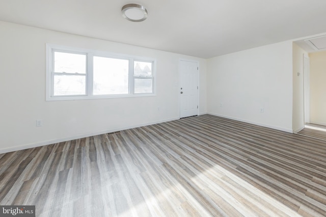 spare room featuring attic access, baseboards, and wood finished floors