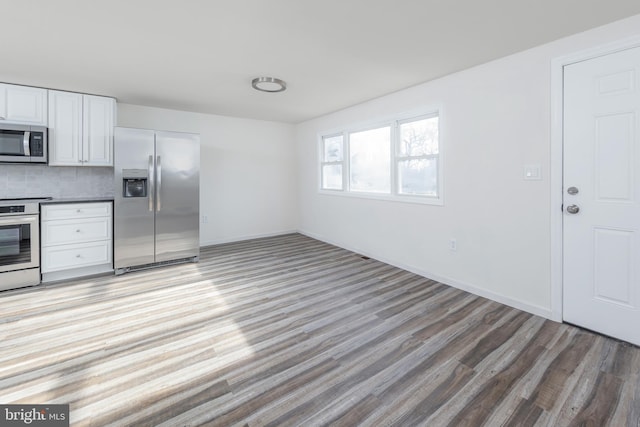 kitchen featuring light wood-type flooring, white cabinets, backsplash, and appliances with stainless steel finishes