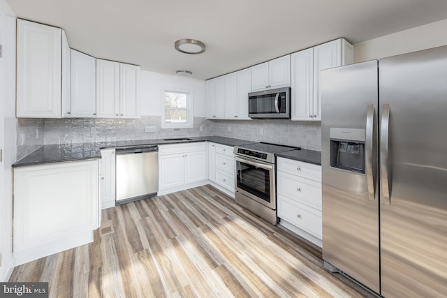 kitchen featuring white cabinets, appliances with stainless steel finishes, tasteful backsplash, light hardwood / wood-style floors, and sink