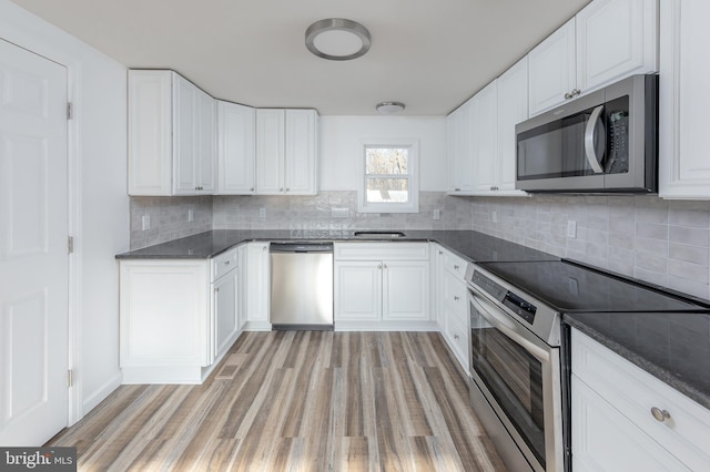 kitchen featuring appliances with stainless steel finishes, white cabinetry, dark stone counters, light hardwood / wood-style floors, and decorative backsplash