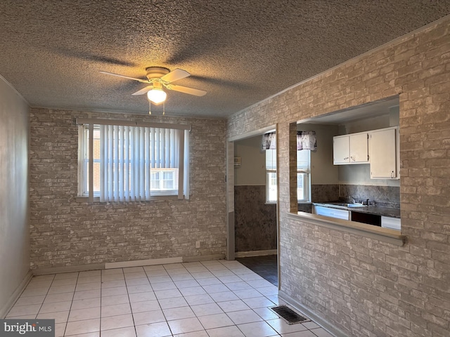 kitchen with sink, white cabinetry, ceiling fan, light tile patterned floors, and brick wall