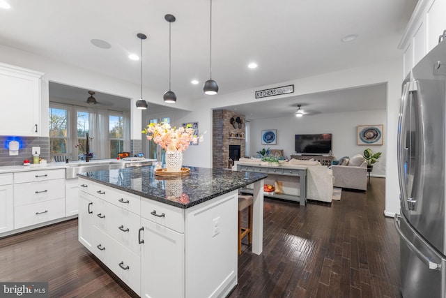 kitchen with white cabinets, a fireplace, stainless steel refrigerator, and a center island