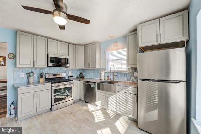 kitchen featuring light stone countertops, light hardwood / wood-style flooring, stainless steel appliances, ceiling fan, and sink