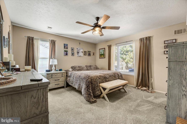 bedroom with ceiling fan, light colored carpet, and a textured ceiling